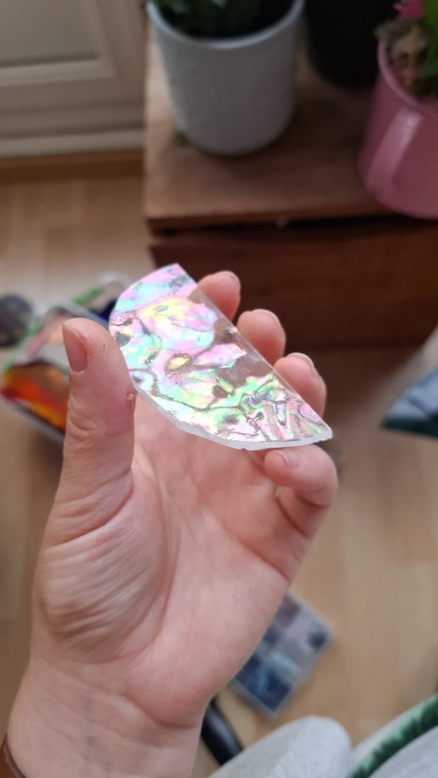 Demi-cercle en verre aux reflets irisés roses, verts et dorés tenu entre les doigts.